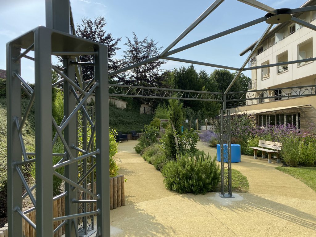 Une pergolas métallique au pied de la résidence. Autour la végétation a déjà trouvé sa place.